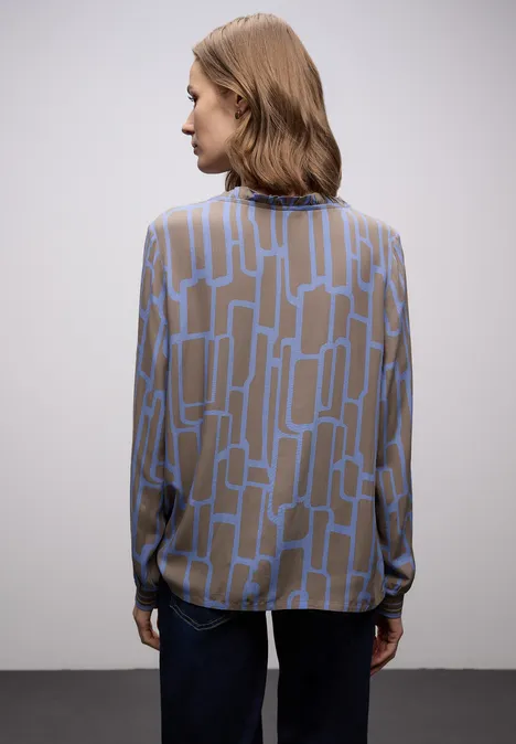 Person von hinten in brauner Bluse mit blauem Muster und dunkelblauer Hose.